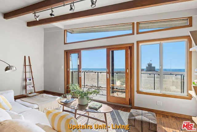 living room featuring beamed ceiling, hardwood / wood-style floors, rail lighting, and a water view