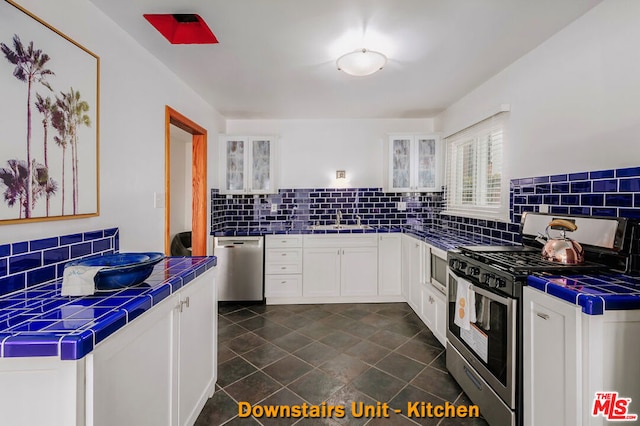 kitchen featuring tile countertops, sink, white cabinetry, and stainless steel appliances