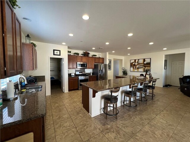 kitchen featuring sink, stainless steel appliances, dark stone countertops, a breakfast bar, and a kitchen island