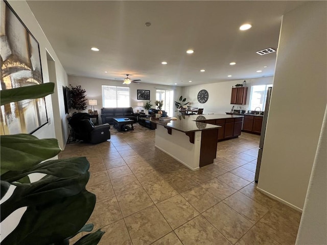 kitchen featuring a kitchen breakfast bar, ceiling fan, sink, tile patterned flooring, and an island with sink