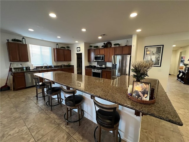 kitchen with a kitchen bar, dark stone countertops, a large island, and stainless steel appliances