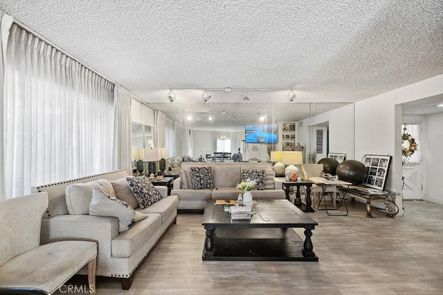 living room with track lighting, a textured ceiling, and light wood-type flooring