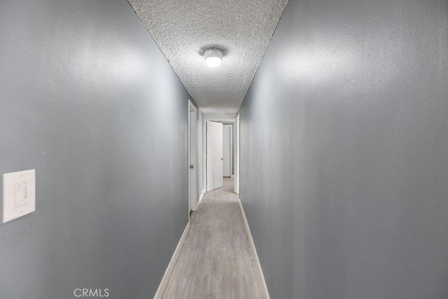 hallway with light hardwood / wood-style floors and a textured ceiling