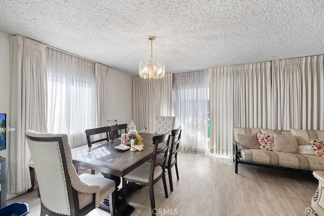 dining area featuring light hardwood / wood-style flooring, a textured ceiling, and an inviting chandelier