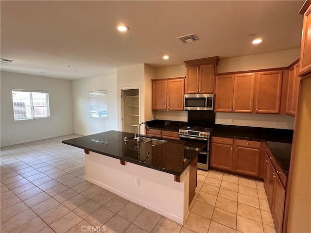 kitchen with sink, an island with sink, dark stone counters, a kitchen bar, and appliances with stainless steel finishes