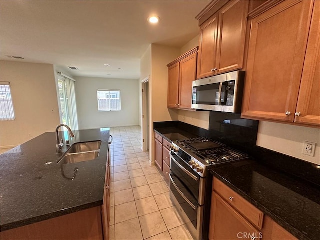 kitchen featuring sink, stainless steel appliances, dark stone countertops, a center island with sink, and light tile patterned floors