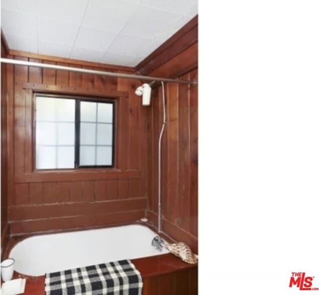 bathroom featuring bathing tub / shower combination and wood walls