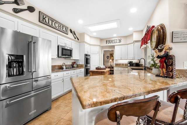 kitchen featuring white cabinets, sink, appliances with stainless steel finishes, light stone counters, and kitchen peninsula