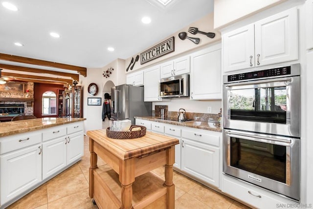 kitchen with light stone countertops, stainless steel appliances, white cabinetry, and light tile patterned flooring