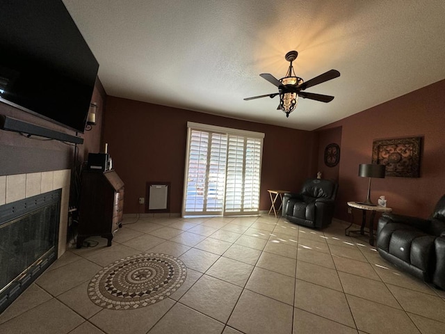 living room featuring light tile patterned floors, a textured ceiling, ceiling fan, and a tiled fireplace