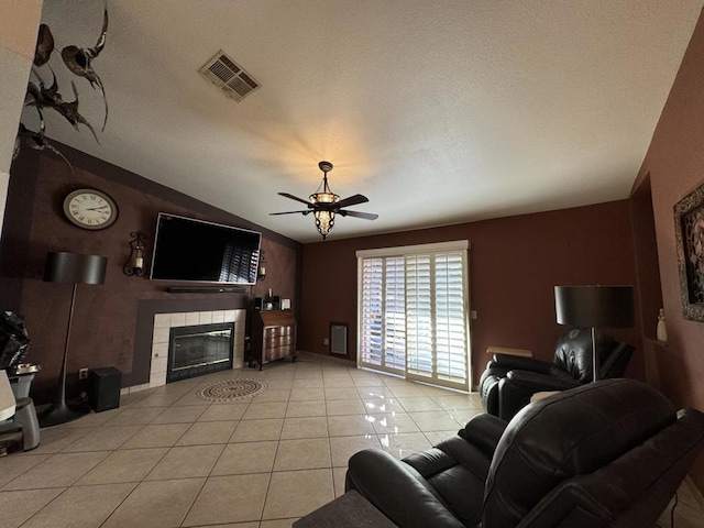 living room with a textured ceiling, ceiling fan, a tile fireplace, lofted ceiling, and light tile patterned flooring