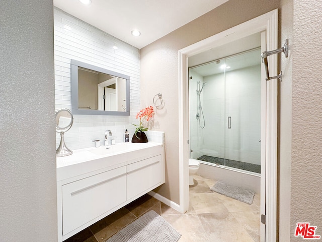 bathroom featuring vanity, toilet, a shower with door, and tasteful backsplash