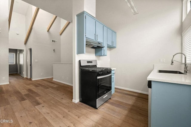 kitchen featuring sink, stainless steel range with gas cooktop, high vaulted ceiling, blue cabinets, and hardwood / wood-style flooring