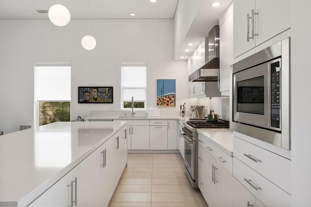 kitchen with sink, wall chimney exhaust hood, stainless steel appliances, decorative light fixtures, and white cabinets