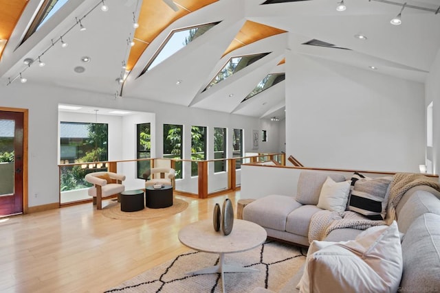 living room featuring high vaulted ceiling, a skylight, track lighting, and light wood-type flooring