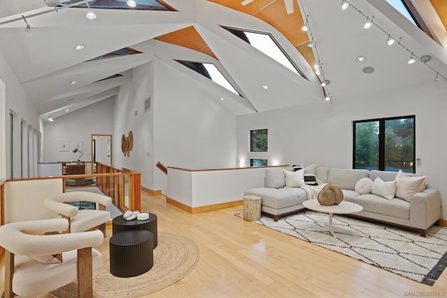 living room with high vaulted ceiling, rail lighting, a skylight, and light hardwood / wood-style floors