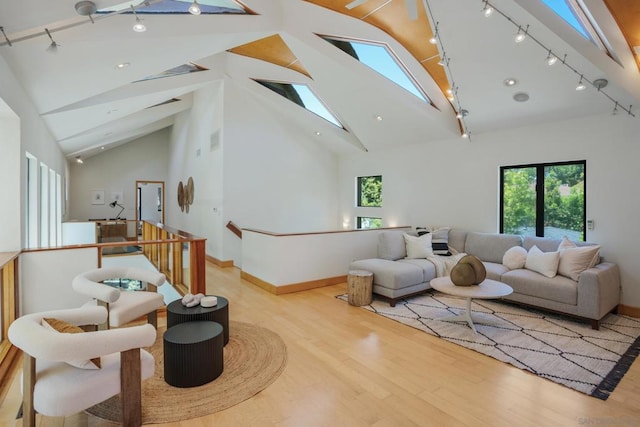 living area with high vaulted ceiling, track lighting, light wood-type flooring, and a skylight