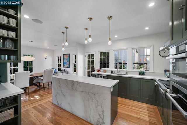 kitchen with appliances with stainless steel finishes, a center island, decorative light fixtures, sink, and light stone counters