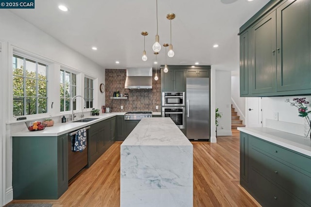 kitchen featuring light stone countertops, pendant lighting, appliances with stainless steel finishes, wall chimney exhaust hood, and decorative backsplash