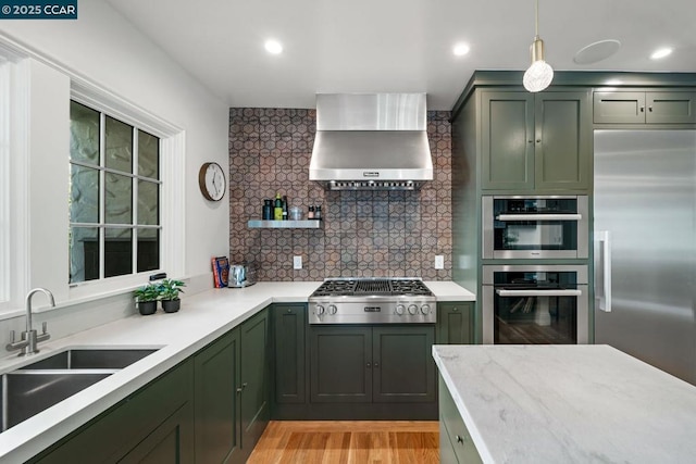 kitchen featuring decorative light fixtures, wall chimney range hood, stainless steel appliances, sink, and backsplash