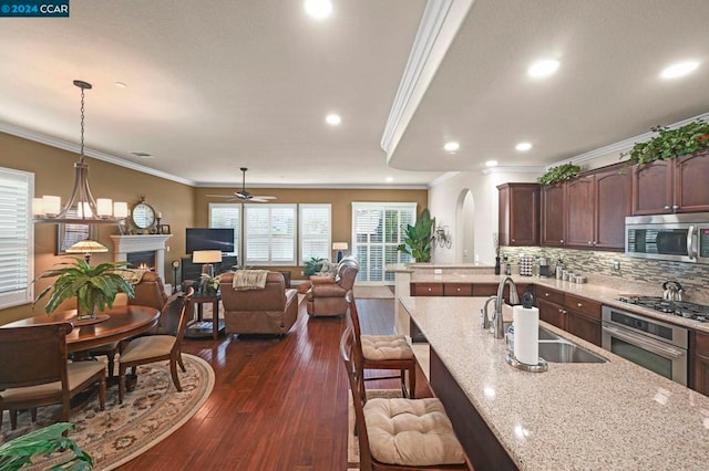 kitchen with appliances with stainless steel finishes, decorative light fixtures, dark wood-type flooring, sink, and light stone counters