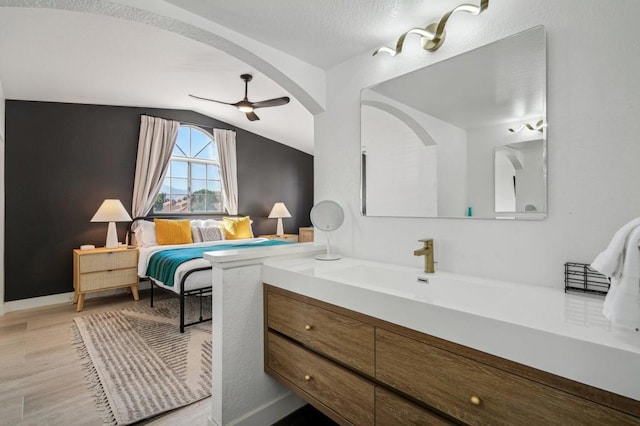 bedroom with lofted ceiling, sink, light hardwood / wood-style flooring, ceiling fan, and a textured ceiling