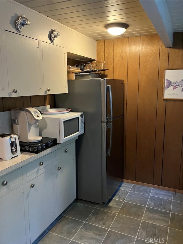 kitchen with stainless steel refrigerator, white cabinetry, dark tile patterned floors, and wood ceiling