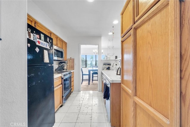 kitchen with gas stove, sink, black refrigerator, and a notable chandelier