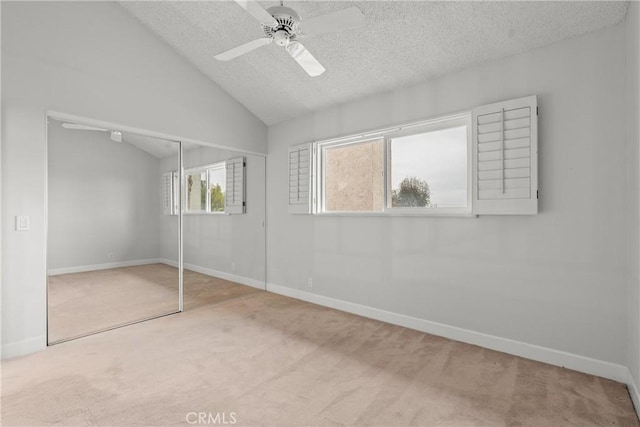 unfurnished bedroom featuring a textured ceiling, lofted ceiling, carpet floors, a closet, and ceiling fan