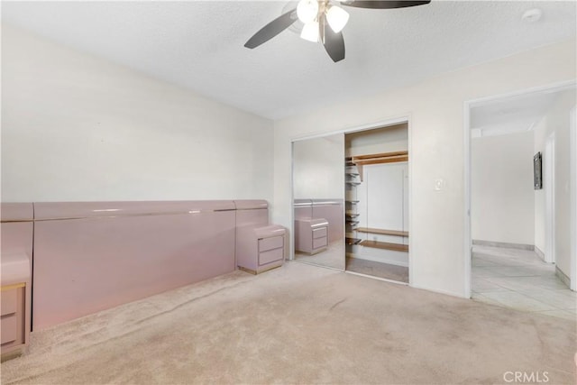 unfurnished bedroom featuring light carpet, a textured ceiling, a closet, and ceiling fan