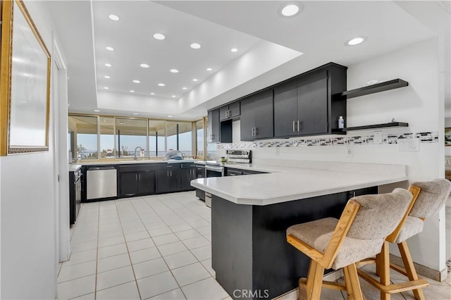 kitchen with sink, stainless steel appliances, kitchen peninsula, a tray ceiling, and a breakfast bar area