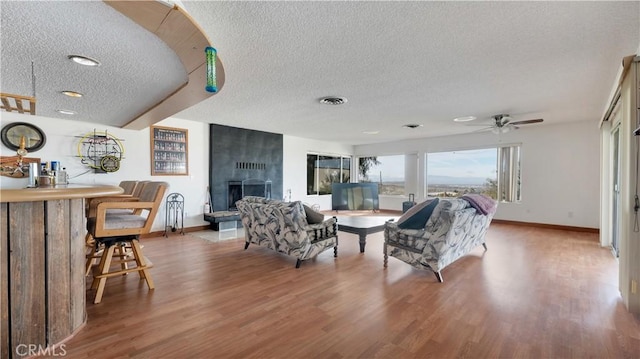 living room featuring hardwood / wood-style floors, a fireplace, ceiling fan, and a textured ceiling