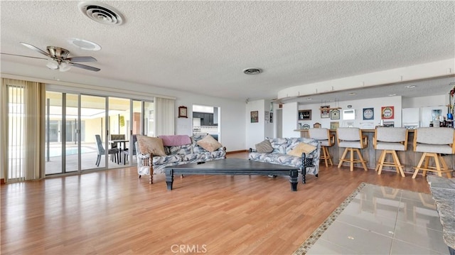 living room featuring ceiling fan, wood-type flooring, and a textured ceiling