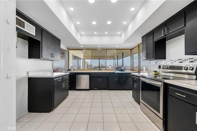 kitchen with a tray ceiling, sink, light tile patterned floors, and appliances with stainless steel finishes