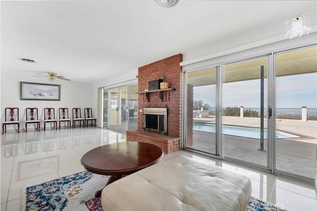 tiled living room with a textured ceiling, ceiling fan with notable chandelier, and a brick fireplace