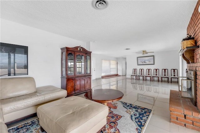 living room with a fireplace, light tile patterned floors, a textured ceiling, and ceiling fan