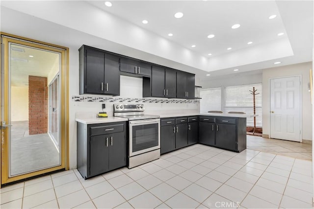 kitchen with kitchen peninsula, backsplash, a raised ceiling, electric stove, and light tile patterned floors