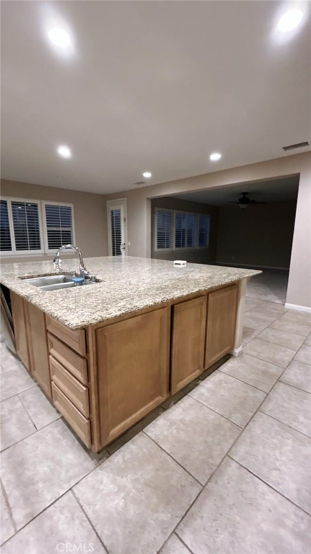 kitchen featuring a center island with sink, light tile patterned floors, sink, and light stone countertops