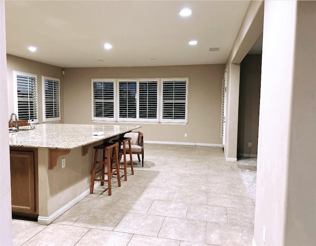 kitchen with sink, light tile patterned flooring, a kitchen bar, and light stone countertops