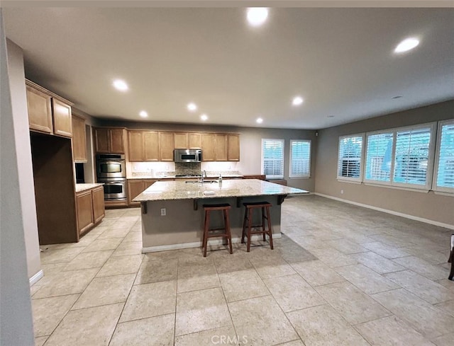 kitchen featuring a center island with sink, appliances with stainless steel finishes, light stone countertops, sink, and a kitchen bar