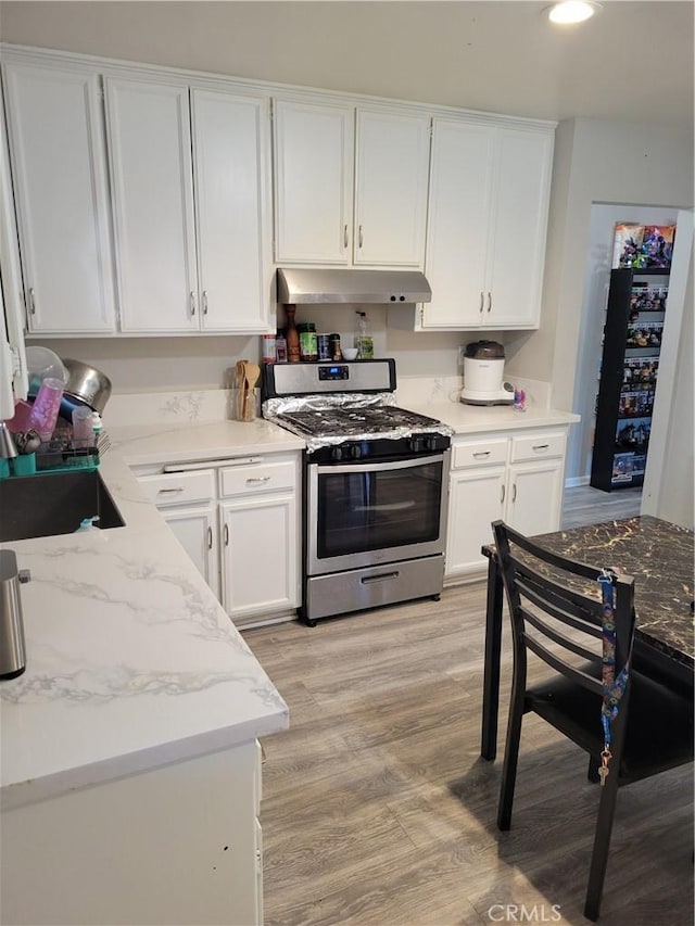 kitchen with stainless steel range oven, white cabinetry, light stone counters, and light hardwood / wood-style flooring