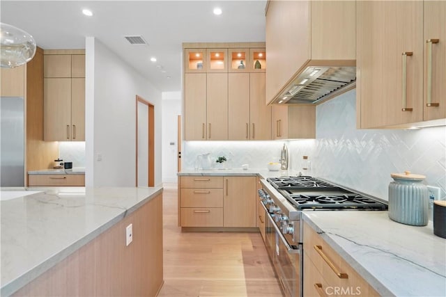 kitchen featuring light brown cabinetry, light wood-type flooring, light stone counters, wall chimney exhaust hood, and premium appliances