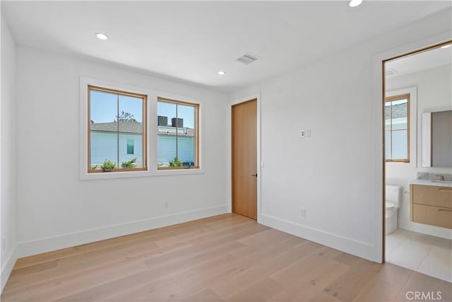 unfurnished bedroom with ensuite bathroom, light wood-type flooring, and sink