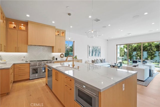 kitchen with light wood-type flooring, stainless steel appliances, a kitchen island with sink, and sink