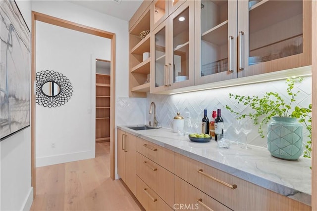 bar featuring light stone countertops, sink, light brown cabinets, decorative backsplash, and light wood-type flooring