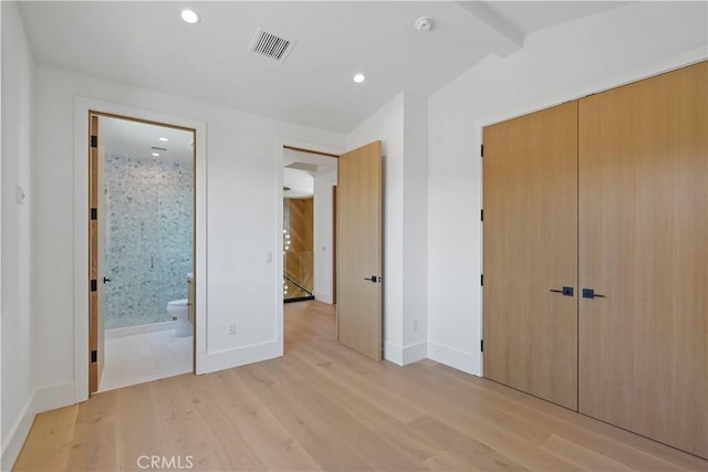 unfurnished bedroom with connected bathroom, a closet, lofted ceiling, and light wood-type flooring