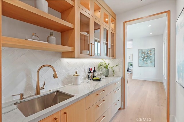 kitchen featuring light brown cabinets, backsplash, sink, light wood-type flooring, and light stone counters