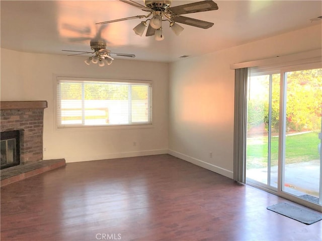 unfurnished living room with ceiling fan, dark wood-type flooring, a healthy amount of sunlight, and a brick fireplace