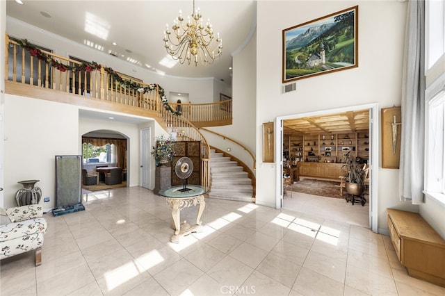 foyer featuring a notable chandelier, a towering ceiling, light tile patterned floors, and ornamental molding