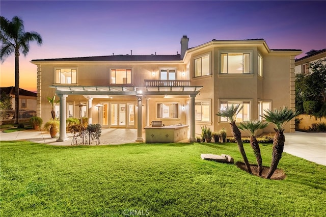 back house at dusk featuring a yard and a pergola